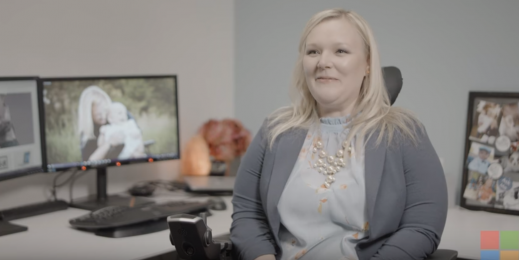 A woman sits in a wheelchair in front of her desk