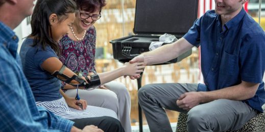 a young girl uses her new robotic hand to shake hands with a man