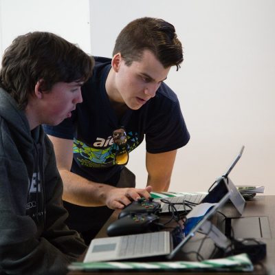 Two young men lean over a laptop screen