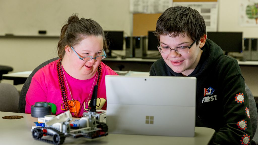 Image of a teenage girl and boy sitting looking at a computer as they design their robot.