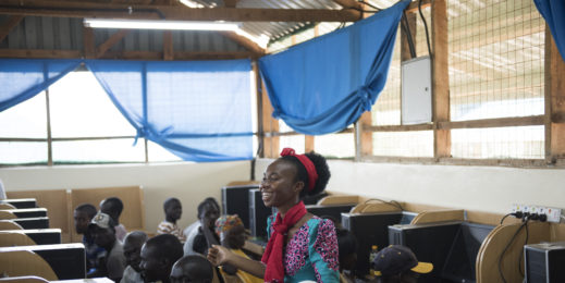 A smiling woman stands amid people sitting at computers