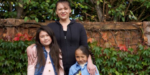 A woman smiles as she stands with her two children in the yard of a home