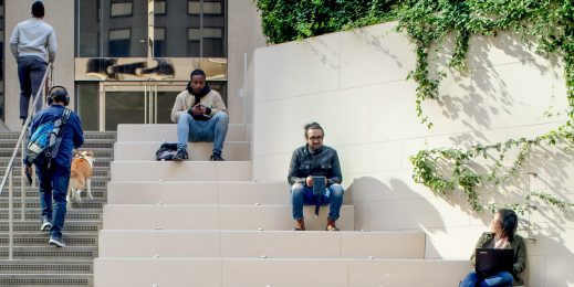 Three people sit on steps and two people walk up steps in front of a building