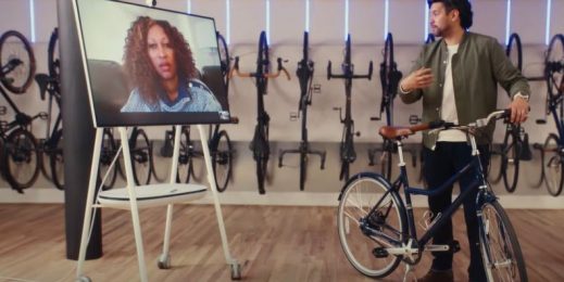 Man with bike talks with woman on a large computer screen