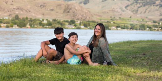 A woman and her two sons sit by a lake