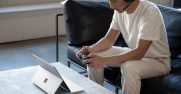 A man sitting down using an Xbox controller with a headset on while on a Surface laptop