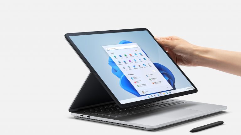 A hand touching a Surface laptop next to a Surface pen