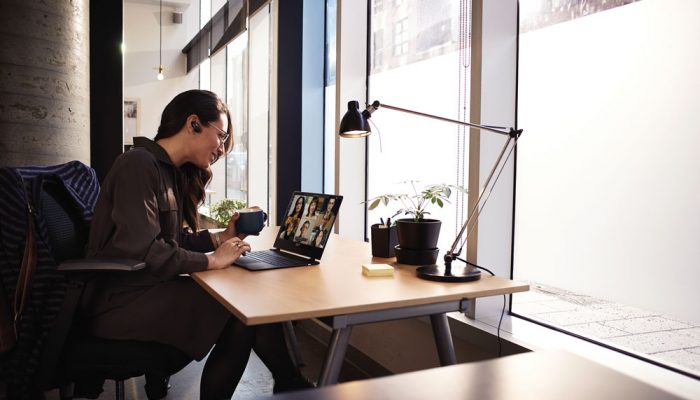 Woman attending a meeting on her laptop computer while holding a cup of coffee