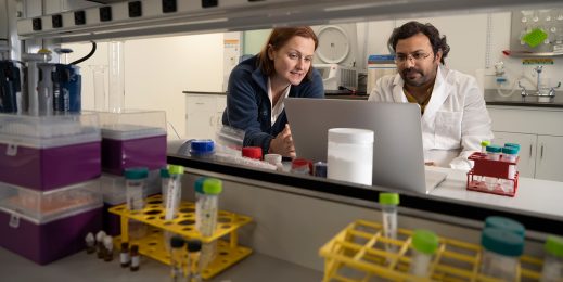 Two people look at a laptop while in a lab