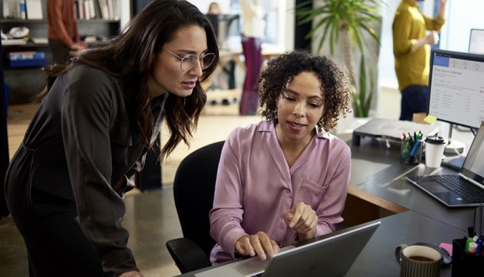 Two women in an office discussing what's on their computer screen