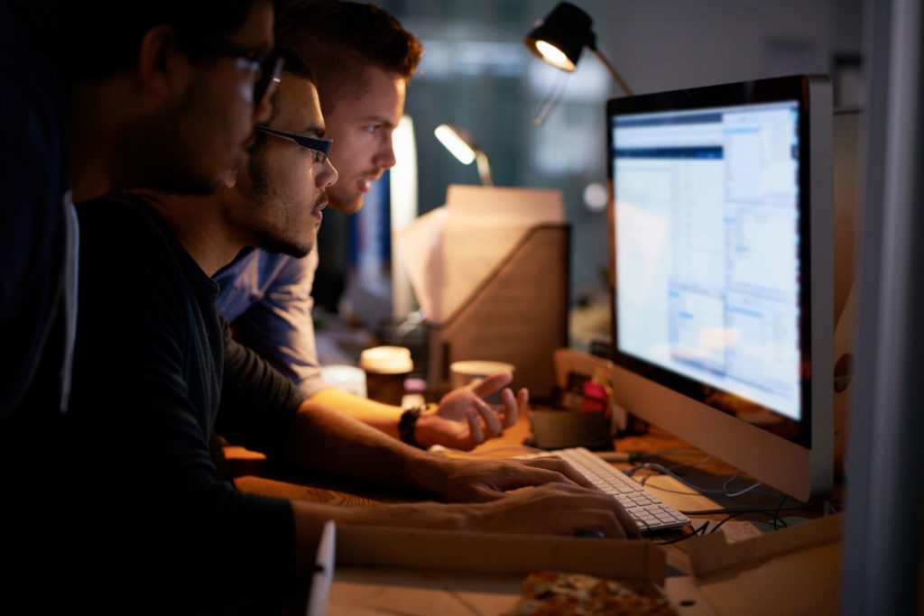 Three men at a desk looking at a computer working on a task together