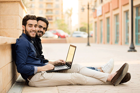 Two people sitting on ground with laptop