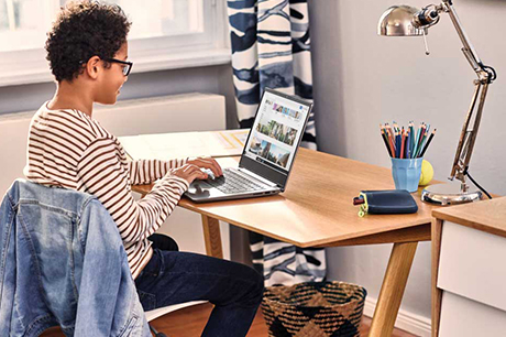 Boy sitting on a chair at his desk at home smiling while using a laptop