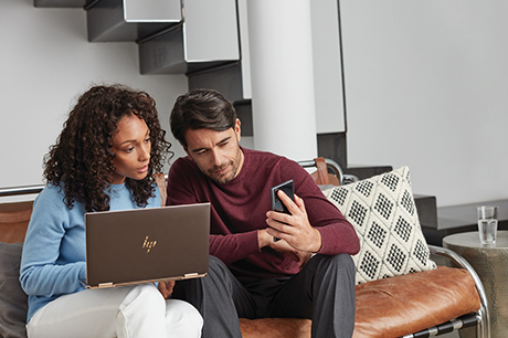 Woman in a blue shirt looking at her laptop and a man in a red shirt looking at his phone.