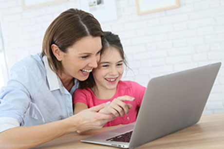 Mother assists her primary-school aged daughter during an online classroom session.