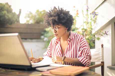 Woman in a white and red striped shirt sitting outside working at her laptop.