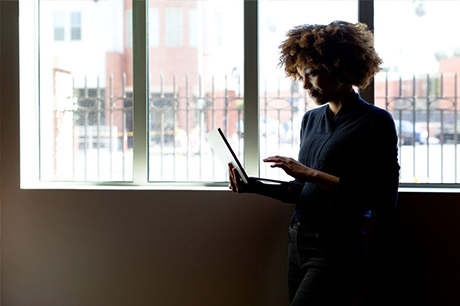 Girl standing next to window looking at laptop