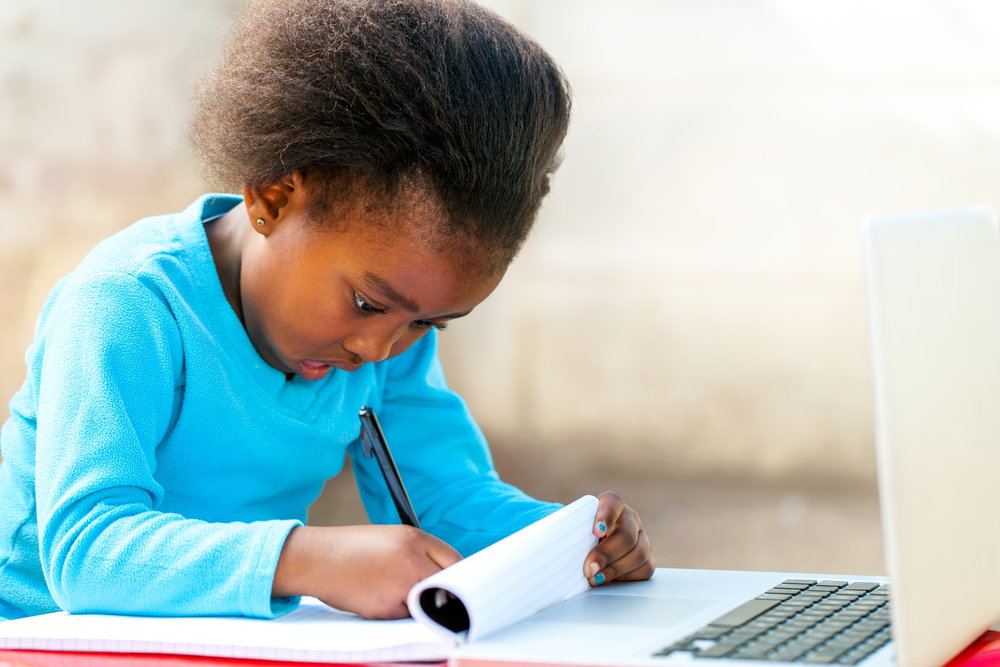 Young primary school girl finishes her homework while attending an online classroom session.