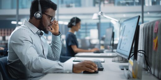 A young security professional takes a call while at work on his desktop computer