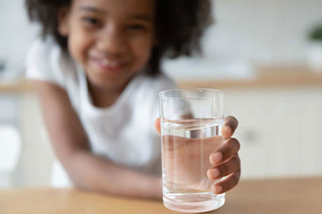 A little girl holding a refreshing glass of water in hand.