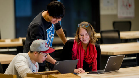 a team of students sit around a laptop