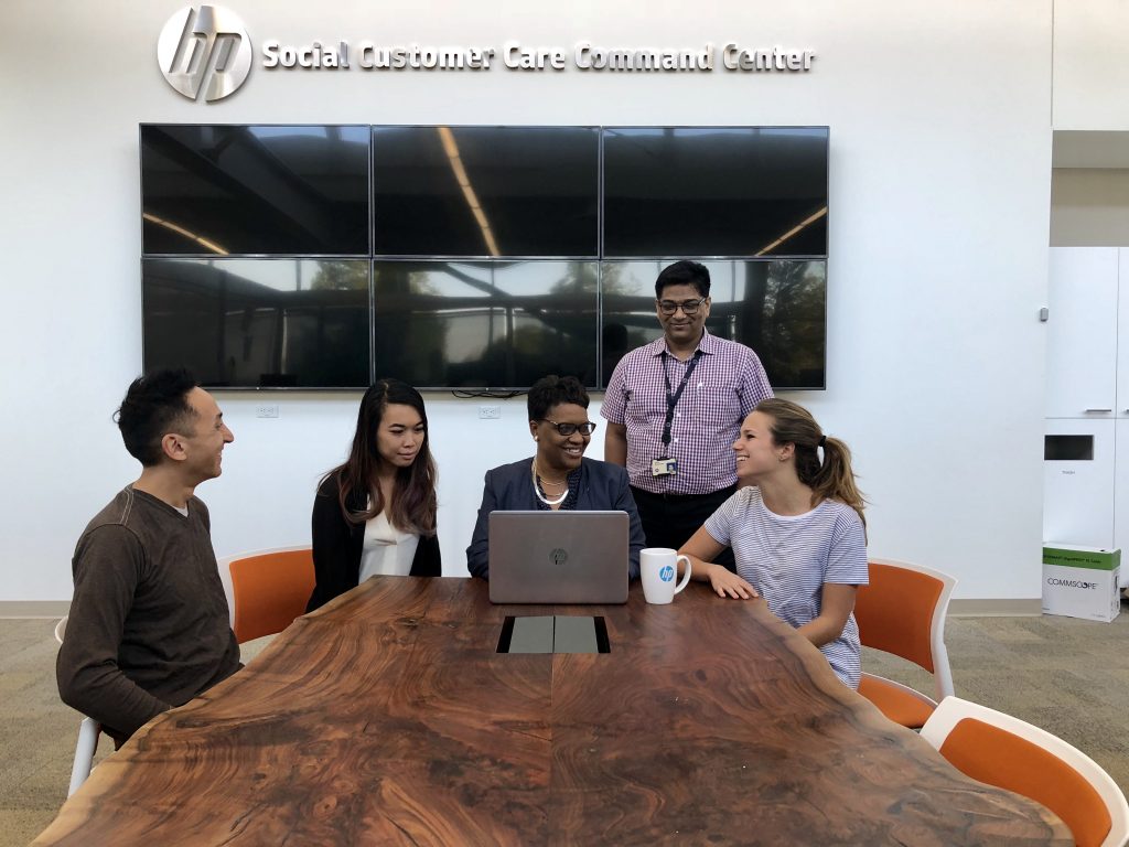 LaChelle Porter-Ainer sits at the end of a long table, in front of a laptop, flanked by four sitting and standing members of her team.