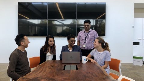 LaChelle Porter-Ainer sits at the end of a long table, in front of a laptop, flanked by four sitting and standing members of her team.