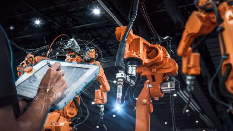 And engineer uses a handheld device to control a robot arm in a smart factory.