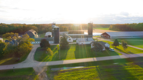 A Wisconsin farm, affiliated with Land O'Lakes, shown from above as the sun casts shadows on the green fields and silos.