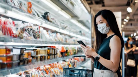 A shopper with a face covering consults her smart phone.