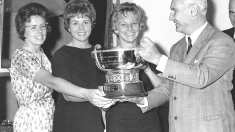 A black-and-white photo shows three women's tennis champions smiling as they accept a trophy for winning the 1963 Fed Cup