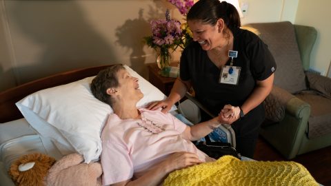 Photo of a caregiver bending over a female hospice patient in a bed.