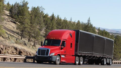 Photo of a red semi truck on a highway lined with trees.