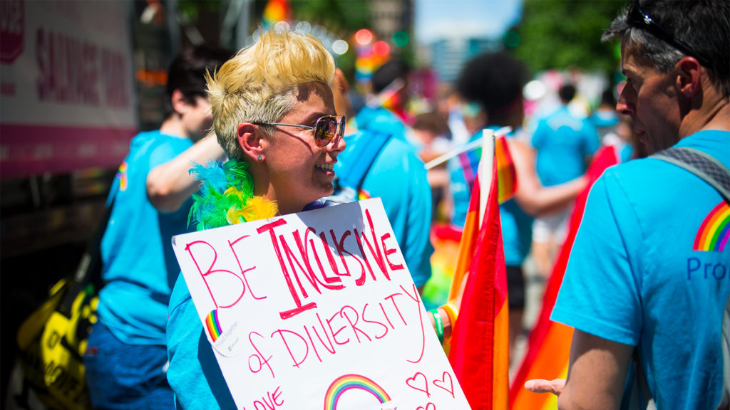 A Microsoft employee at the Seattle Pride Parade holding a sign that says "Be Inclusive."