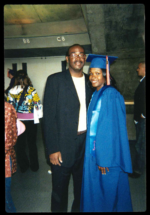 Heather Dowdy wears a blue graduation cap and gown while she and her father, Martin Royce, smile for the camera at her college graduation ceremony.