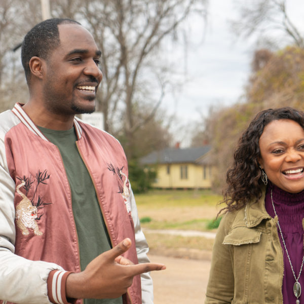 A man and a woman laugh together as they stand outside a vacant lot