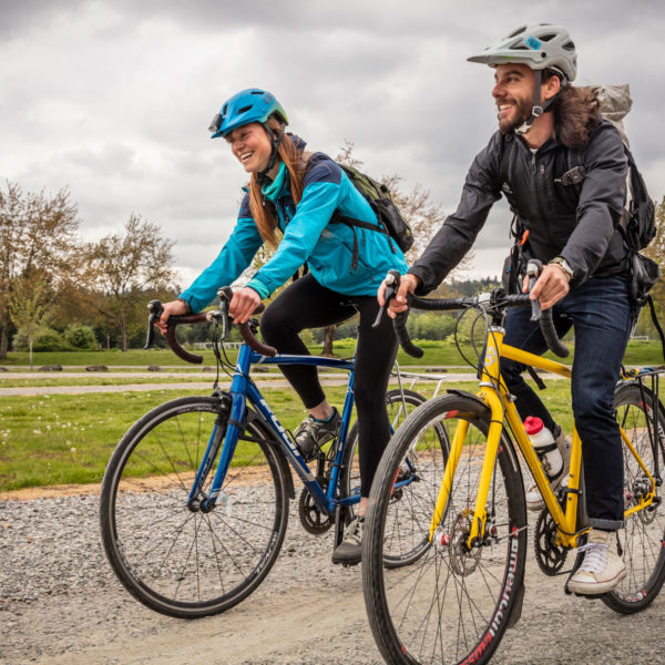 A man and a woman each ride a bike on a gravel trail