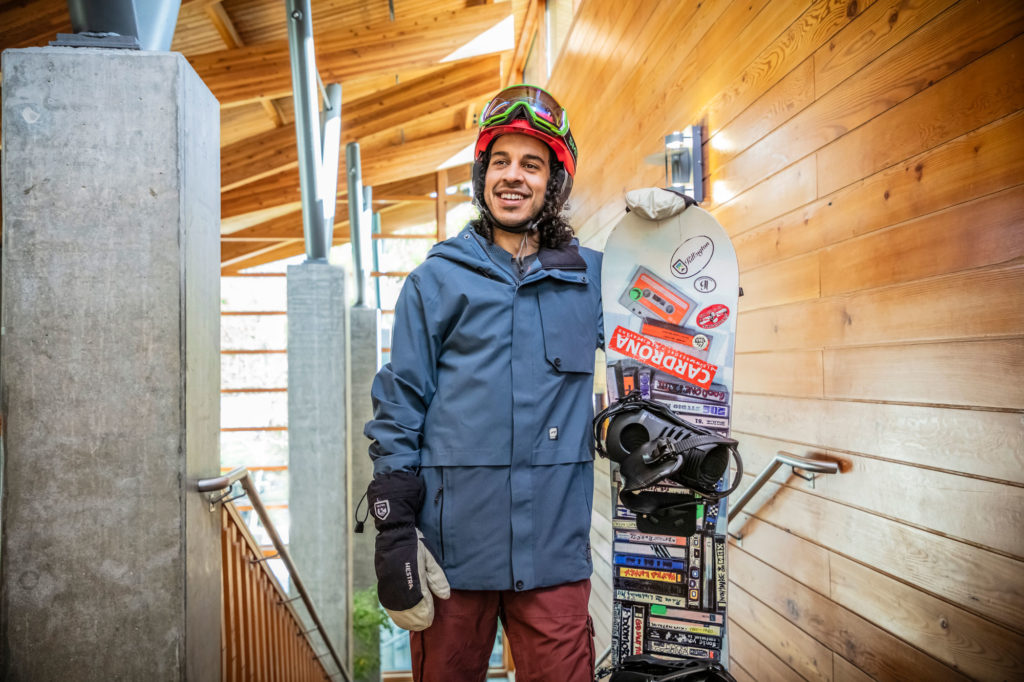 A man stands holding a snowboard while wearing snowboarding gear