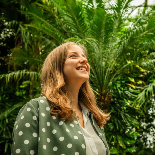 a woman looks up at a blue sky with green palm trees in the background