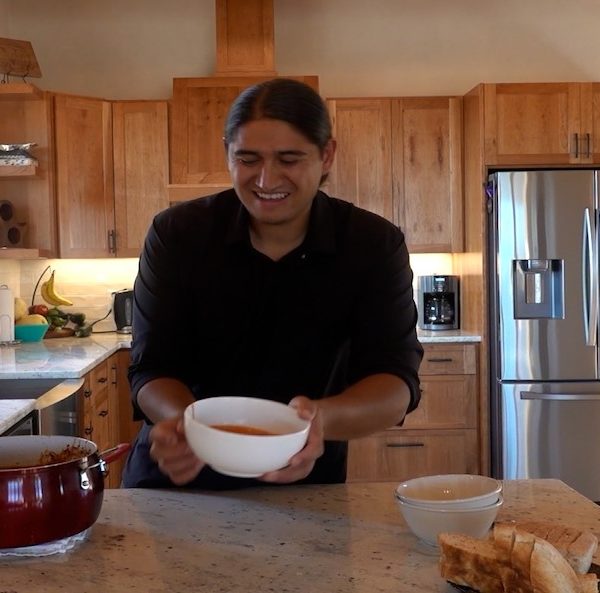 A man serving a bowl of chile in his kitchen