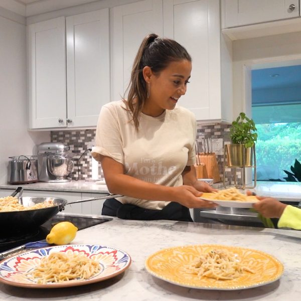 A woman stands in her kitchen and prepares plates of pasta.