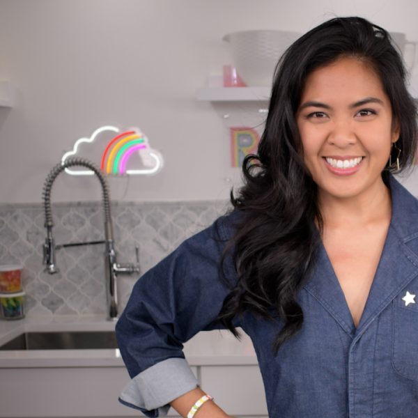 A woman in a woman smiling as she stands in front of a kitchen sink