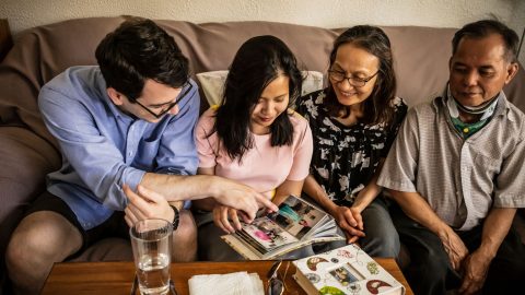 Huong Haley sitting on a couch with her husband and her parents, looking at scrapbook photos together