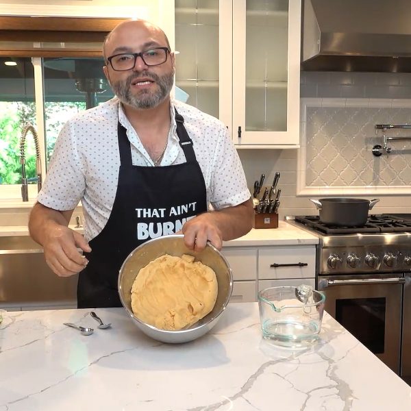 A man wearing an apron holds a pan of dough