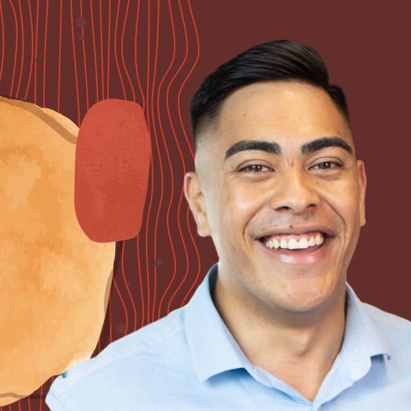 Dylan wearing a blue button-down shirt and smiling in front of a brown background with colorful hues.