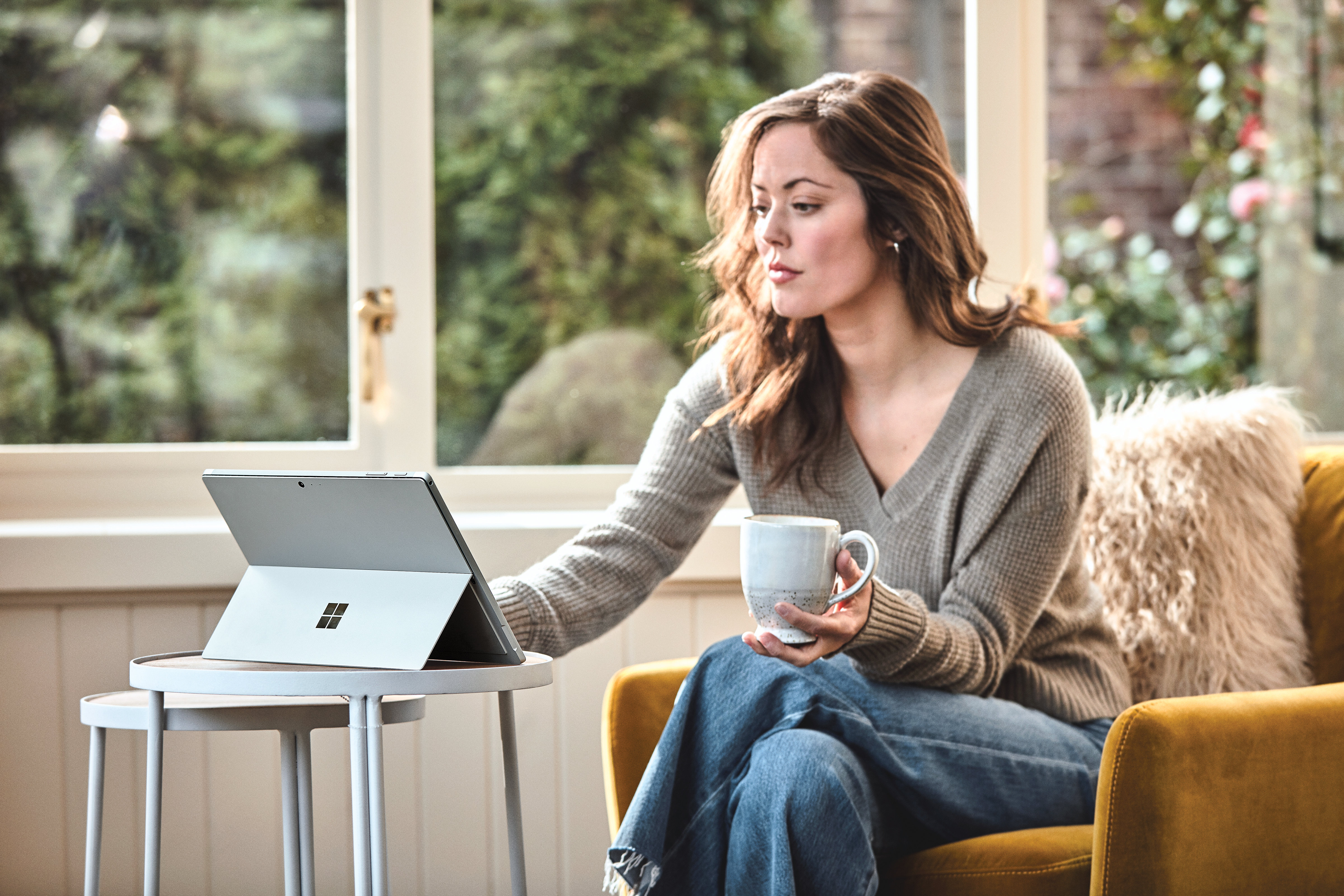 Eine Frau sitzt auf einem Sessel und arbeitet mit dem Surface Pro 6.