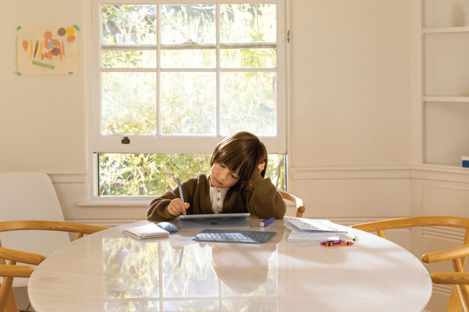 Datenschutz und Datensicherheit in Bildungseinrichtung. Kind das an einem Tisch zu Hause an einem Surfacegerät Schularbeiten erledigt.