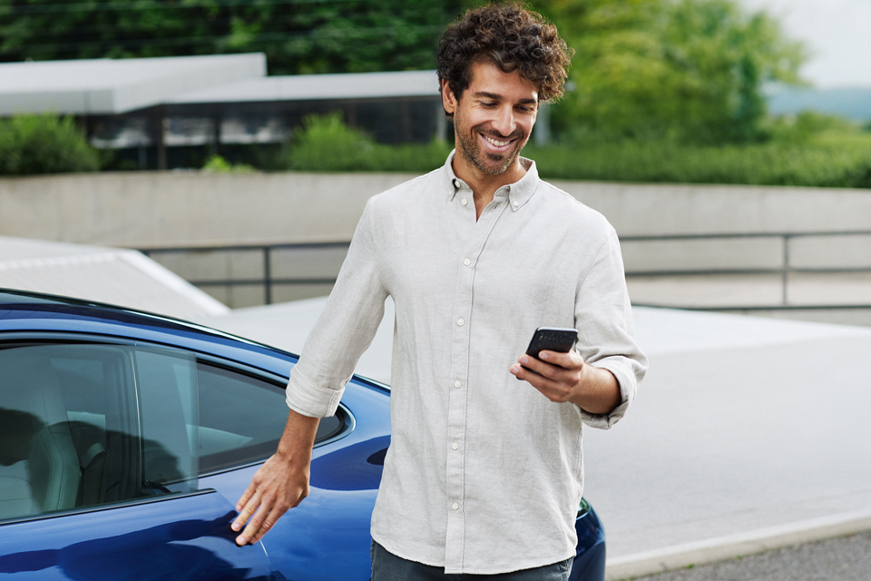 Mann mit Smartphone in der Hand steht vor blauem Porsche