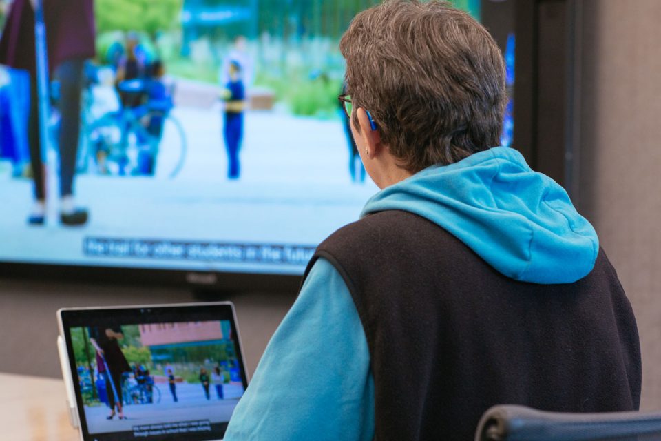 Eine Frau sitzt vor einem Laptop und schaut auf eine große Leinwand