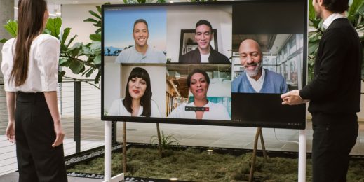 Eine Frau und ein Mann stehen vor einem Surface Hub 2S und nehmen an einem hybriden Teams-Meeting teil